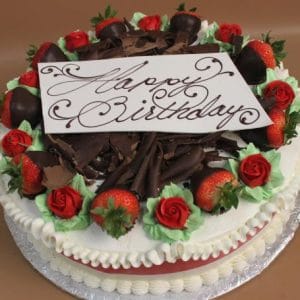 BD-020 is a birthday cake adorned with chocolate-covered strawberries, red icing roses, chocolate shavings, and a white chocolate plaque displaying "Happy Birthday" in elegant script.