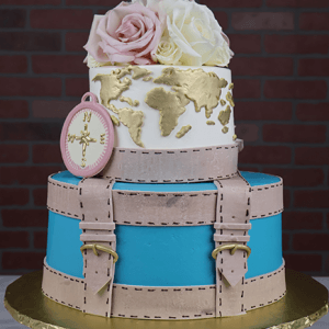 The BR-000B is a two-tiered cake featuring a blue and beige suitcase base, world map and compass on the top tier, pink and white roses on top, displayed on a gold base with a brick wall background.