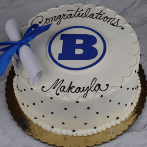 A round white GC-001A Braintree High School cake with a blue B emblem, black "Congratulations Makayla" icing, and a white diploma with blue ribbon on a gold board.