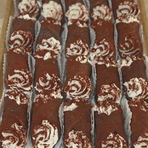 Rows of CO-082 Chocolate dipped cannolis filled with white cream are neatly arranged on a tray, each resting in a paper holder.