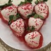 VC-032 White chocolate dipped strawberries: Six strawberries coated in white chocolate, drizzled with pink icing, topped with red heart-shaped sprinkles, and presented in red paper cups on a silver platter.