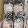 A tray of CO-081 Chocolate filled Cannolis, dusted with powdered sugar and arranged neatly in paper liners.