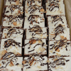 CO-084 Almond Joy Squares: chocolate cake squares topped with whipped cream, sliced almonds, and drizzled chocolate, arranged neatly in a tray.