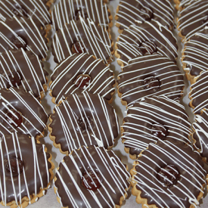 Rows of CO-046 Tea cookies dipped in chocolate, each topped with glossy raspberry jam and finished with a diagonal white chocolate drizzle, neatly arranged on a parchment-lined surface.