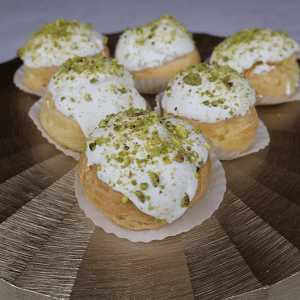 Pistachio Cream Puffs topped with white icing and crushed pistachios, arranged on a gold, striped platter.