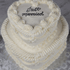 The BR-000A is a white, three-tiered heart-shaped cake with ornate icing borders and "Just married" written in black icing on the top layer, displayed on a silver patterned surface.