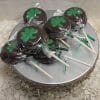 STP-027 Chocolate dipped Oreos, decorated with green shamrock shapes and wrapped in clear plastic, are displayed on a silver stand with a decorative edge on a white textured surface.