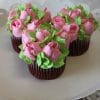 Three CC-086 chocolate cupcakes with white filling, decorated with pink and green frosting to look like blooming roses and leaves, arranged on a white cake stand.