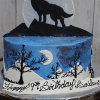 The CB-012P is a round cake featuring a howling wolf silhouette against a large moon, mountain shapes, and tree silhouettes. "Happy 17th Birthday Sailor" is written in black script icing.
