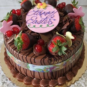 Black Forest Cake topped with chocolate-dipped strawberries, red cherries, chocolate shavings, pastel bunny shapes, and a pink “Happy Easter” disc in purple icing. Presented on a gold base.