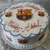 The ST-007A Futbol Club Barcelona round white cake features FC Barcelona logos, blue piping, and "Happy Birthday Hubby - Abdul" in red on top. It sits on a silver board over a floral tablecloth.
