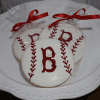 Three CE-002b sports cookies, round and designed as baseballs with red stitching and a bold red "B" in the center, individually wrapped in clear plastic with red ribbons, are displayed on a white plate.