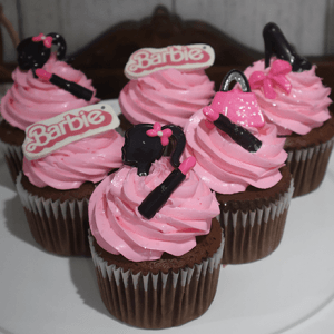 Five CC-030A chocolate cupcakes with white chocolate mousse filling, topped with Barbie-themed decorations—logos, silhouettes, high heel, purse, and lipstick—are arranged on a white plate.