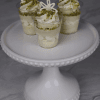 Three CO-103 Pistachio Shooters, small dessert cups of creamy white mousse topped with crushed pistachios and white chocolate decor, are displayed on a cake stand against a marble background.