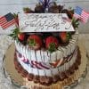 The JC-011 Strawberry Grand Marnier is a festive cake topped with chocolate strawberries, American flags, and a “Happy July 4th” topper, featuring red, white & blue accents plus piped chocolate frosting on a glass plate.