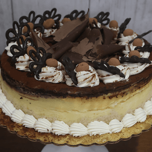 The GD-015 Tiramisu Cheesecake is a round layered cake topped with whipped cream, chocolate shavings, cocoa-dusted candies, and chocolate decorations, presented on a gold cake board against a wooden background.