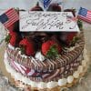 The JC-004 Chocolate/Oreo cake features chocolate-covered strawberries, chocolate shavings, and U.S. flags, topped with a "Happy July 4th" sign and festive decorations, and wrapped in a red, white, and blue ribbon.