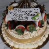 The NY-003 Pina Colada cake is a festive treat topped with chocolate-dipped strawberries, shredded coconut, gold ribbon, and a “Happy New Year 2025” plaque featuring star and champagne glass decorations.