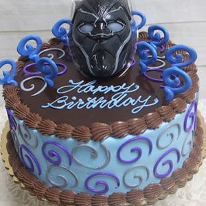 A round birthday cake with blue and brown frosting, purple and blue swirls, “Happy Birthday” written in icing, and topped with an SC-081 Black Panther plastic mask cake topper.