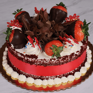 The BD-006B Red Velvet is a round cake topped with chocolate-dipped strawberries, chocolate shavings, red velvet crumbs, piped whipped cream, colorful sprinkles, red decorative pieces, and presented on a gold cake board.