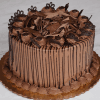 The BD-014C Chocolate/Chocolate cake is round, set on a gold base, and features chocolate frosting, curls, piped swirls, chocolate accents, and drizzled sides. It is displayed on a marble surface.