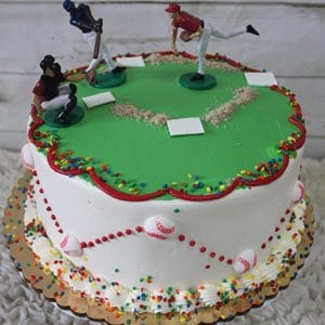 The SC-071 Baseball is a round cake decorated like a baseball field with white frosting, red piping, sprinkles, small baseball designs on the sides, and plastic player figurines on top.