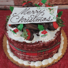 The CH-007 Display Red Velvet with Christmas Decor is a festive Christmas cake topped with chocolate strawberries, whipped cream, holly leaves, and a Merry Christmas white chocolate plaque on a gold cake board.