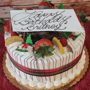 The CH-005 Display Gold Cake features lemon raspberry filling, festive Christmas decor, and a gold finish. It’s topped with strawberries, lemon slices, cream, chocolate drizzle, and a “Happy Birthday Britney” plaque in cursive.