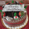The CH-004 Display Chocolate Cake with Oreo Mousse features chocolate-dipped strawberries, holly leaves, whipped cream, and a white chocolate "Merry Christmas" plaque, elegantly presented on a red textured surface.