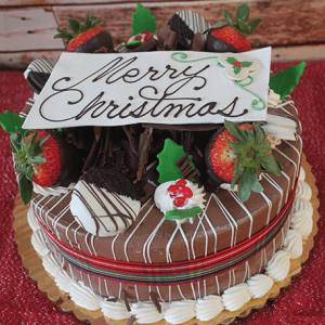 The CH-004 Display Chocolate Cake with Oreo Mousse features chocolate-dipped strawberries, holly leaves, whipped cream, and a white chocolate "Merry Christmas" plaque, elegantly presented on a red textured surface.