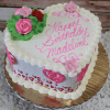 The VC-013A is a heart-shaped cake featuring pink and red flowers, green leaves, white icing borders, pink heart designs, and "Happy Birthday Madeline" written in pink icing.