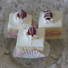 Three square pieces of AP-045H Lemon Raspberry Squares, layered with vanilla and pink sponge cake and white frosting, each topped with a strawberry and drizzled with white chocolate, are displayed on a glass plate.