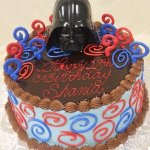 A round SC-007 Darth Vader cake with chocolate frosting, blue and red swirl designs, a Darth Vader helmet topper, and "Happy 18th birthday Shanie" written in red icing.