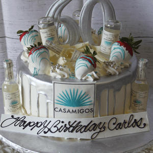 The BD-024S Casamigos is a white birthday cake with silver accents, white chocolate-dipped strawberries, mini Casamigos tequila bottles, a "Happy Birthday Carlos" message, and a large silver "60" topper.
