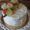 The BR-003 cake features white textured frosting, topped with white and orange roses plus lemon and orange slices, and is displayed on a white decorative stand with a gold base.