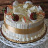The BD-018P Mimosa Torte is a round cake with white chocolate shavings and strawberries on top, finished with white frosting, orange icing lines, and a gold ribbon around the sides, presented on a white ornate stand.