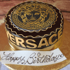 The BD-033 Designer Ganache/Gold is a round chocolate cake with the gold Versace logo and Medusa head on top, Versace lettering on the side, and a white "Happy Birthday" card in elegant script.