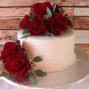 The THX-037 is a white frosted cake adorned with red roses and green leaves, presented on a silver cake board against a rustic wooden backdrop.