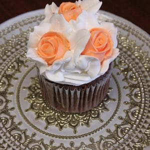 CC-014 Chocolate with white chocolate mousse filling, topped with white frosting and three orange buttercream roses, is displayed on an ornate silver-patterned plate.