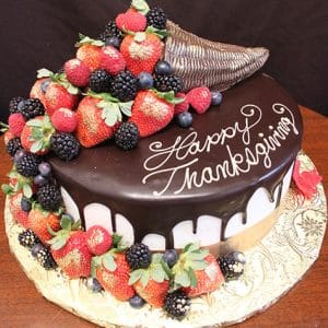 The THX-028 is a round chocolate-dripped cake topped with a cornucopia of strawberries, blackberries, and raspberries, featuring "Happy Thanksgiving" written in white icing.