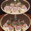 A two-tiered gold dessert stand displays ST-001 Milk Chocolate Strawberries, each in a white paper cup with chocolate drizzle, arranged neatly on both tiers.
