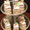 A two-tiered gold tray displays Carrot Squares—small square slices topped with white icing and a decorative frosting carrot.