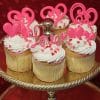 The VC-037 Display Valentine gold cupcakes feature chocolate mousse filling, white frosting, pink heart-shaped "Love" decorations, and are arranged on a gold tiered stand against a red heart-patterned background.