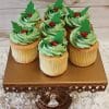 The CC-076 Gold cupcake features chocolate filling and holly berry decor, displayed on a gold ornate stand with crystal accents against a white textured surface and wooden wall background.
