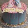 The BB-024 features a blue cake with pink icing drip, colorful sprinkles, and fondant baby shoes—one pink, one blue. A card on top reads "Shower of Joy Girl or Boy" in yellow icing.