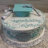 GC-016 is a round graduation cake with teal and silver icing, topped with a fondant cap, diploma, "Congratulations Delya" written on top, and the year 2018 displayed on the side.