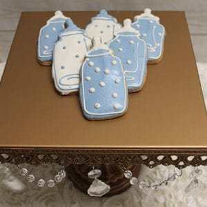 CE-004b baby shower blue and white bottle-shaped cookies with icing are displayed on a gold stand adorned with hanging crystal beads.