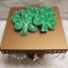 The STP-001C St. Patrick’s Day set features green shamrock cookies with white icing on a gold pedestal stand with crystals, displayed on a white textured surface and pale wood background.