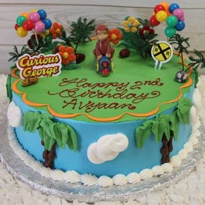 A vibrant SC-043 Curious George birthday cake features a George figurine, balloons, palm trees, flowers, and clouds. "Happy 2nd Birthday Avyaan" is written in red icing.
