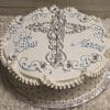 RC-023 is a round white cake with a silver cross, blue swirls, white flowers, "God Bless Marcus" inscription, ruffled edges, and silver edible pearls around the sides.